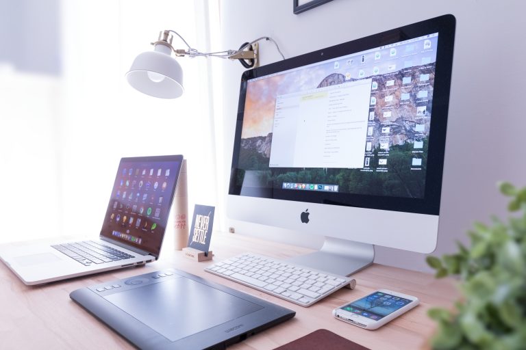 Escritorio moderno con iMac, laptop, tableta gráfica y smartphone sobre una mesa de madera.