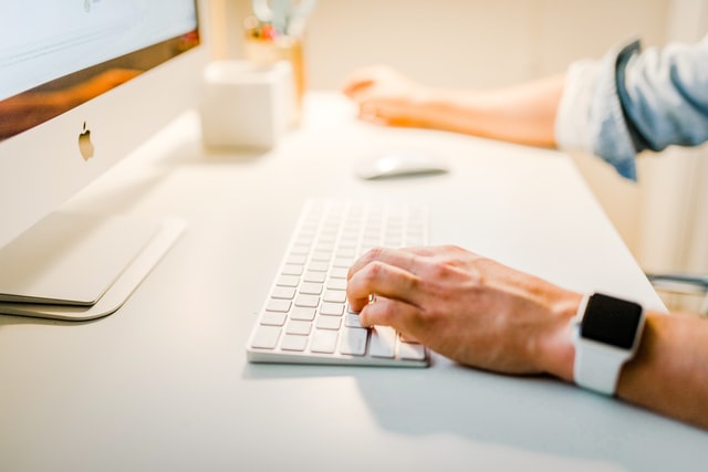 Mano escribiendo en teclado de computadora en un escritorio minimalista y moderno.