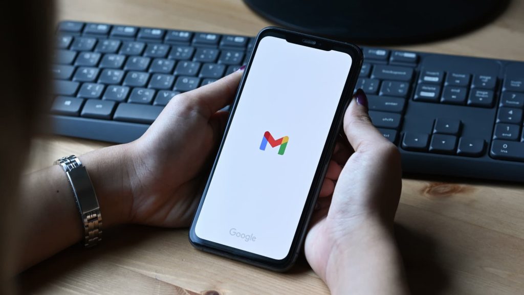 Mujer sosteniendo un teléfono con la app de Gmail abierta sobre un teclado.